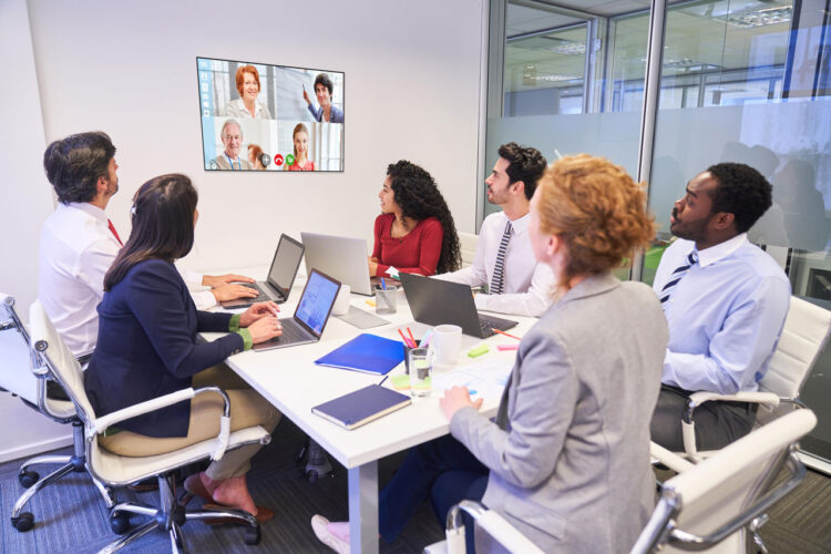 People sitting in a meeting room, looking at a splitted wall screen, using Kramer VIA 4
