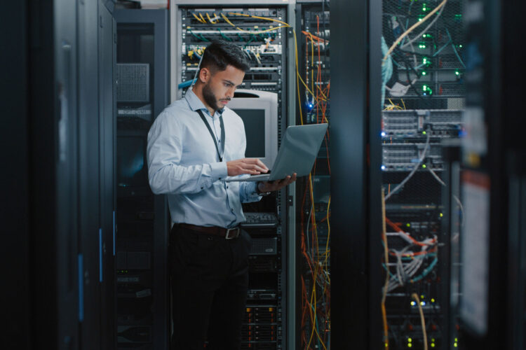 A man standing with a computer in a server room